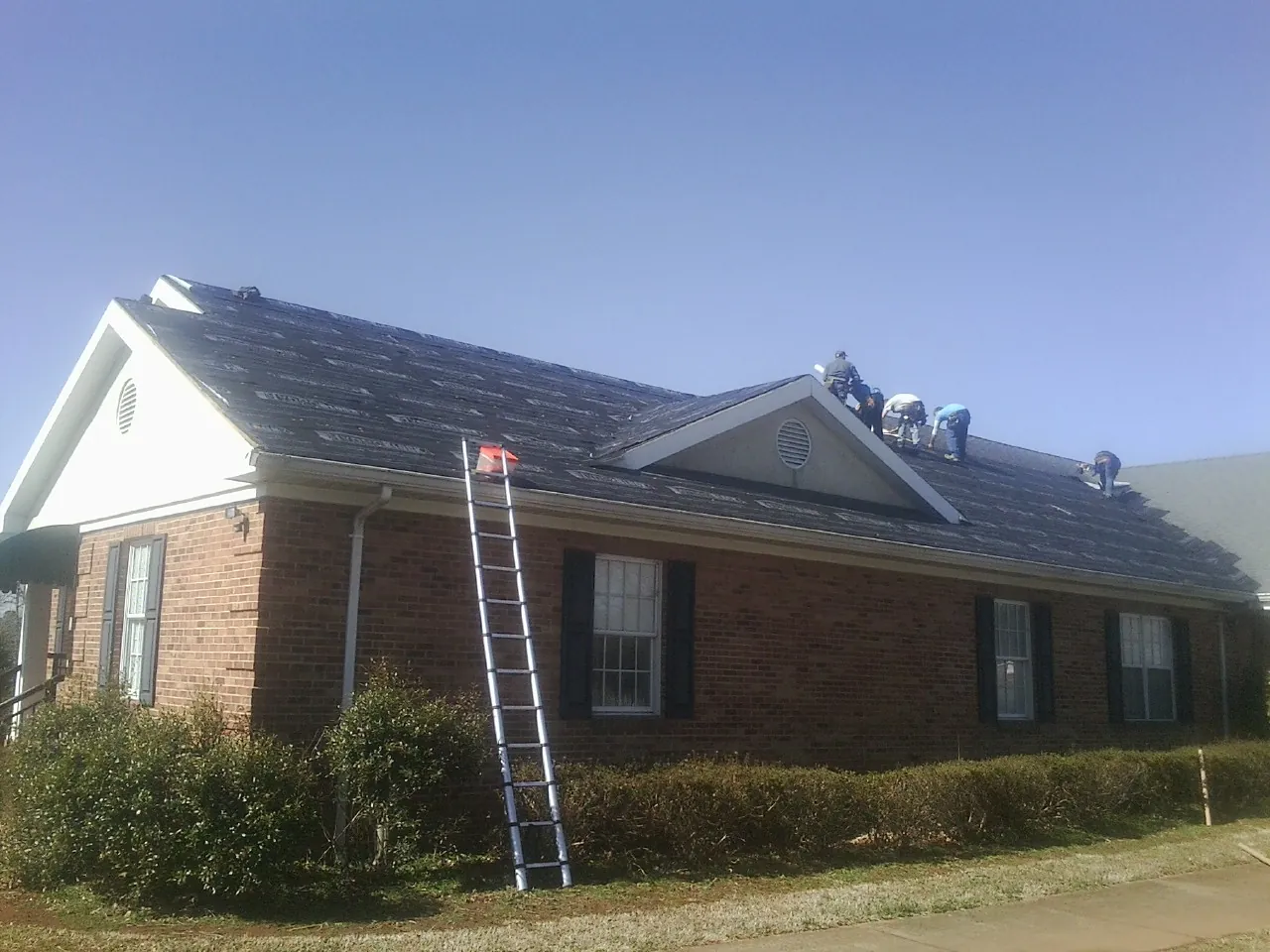 Crew tearing shingles off a brick ranch roof with a ladder set — Metal Roof Repair work by our crew in Liberty